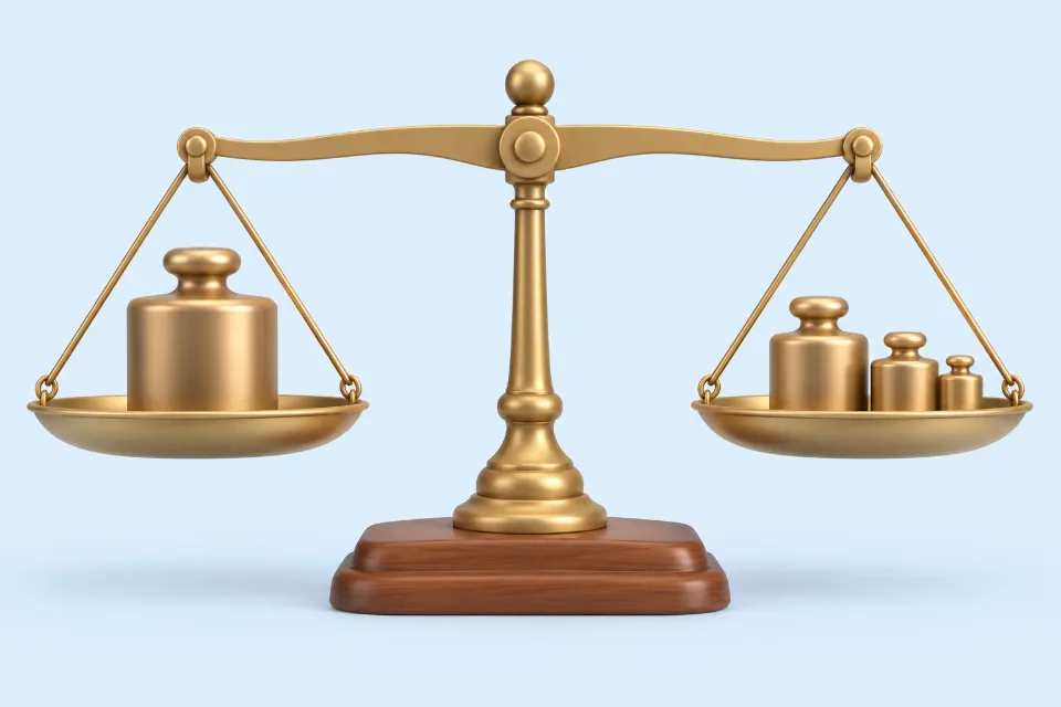 An old-style balance scale in balance, with one large block weight on the left pan and several smaller round weights on the right pan.